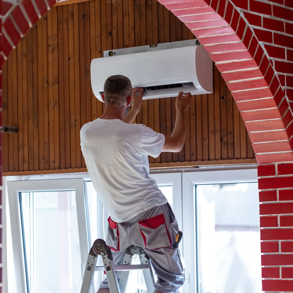 Un technicien procède à l’installation d’un climatiseur dans le salon d’un appartement.