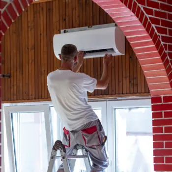 Un technicien procède à l’installation d’un climatiseur dans le salon d’un appartement.