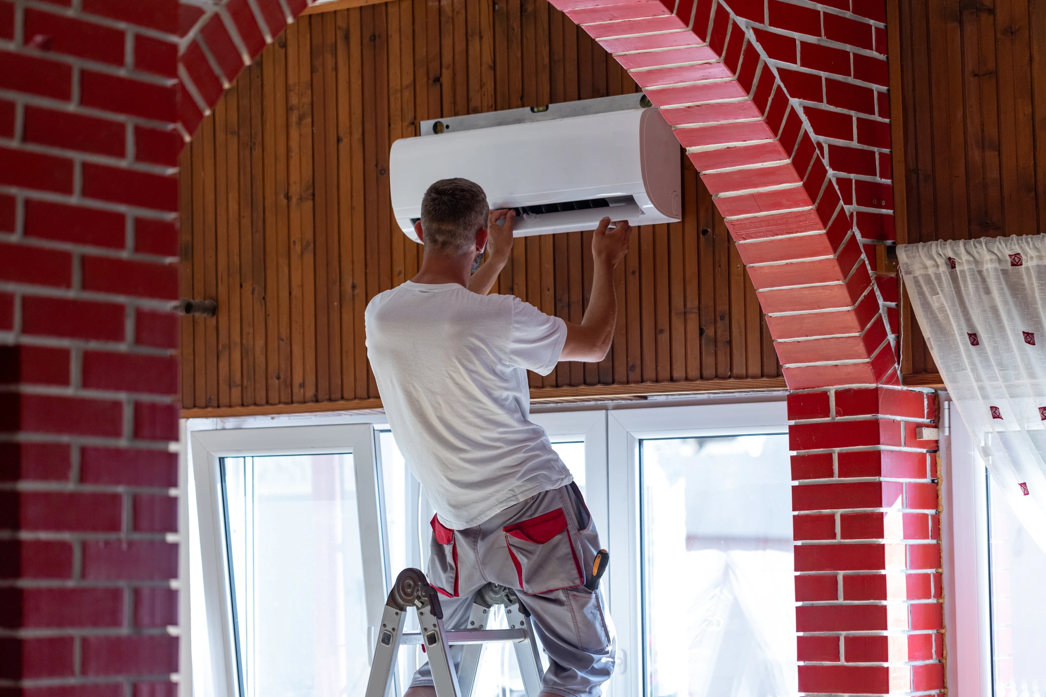 Un technicien procède à l’installation d’un climatiseur dans le salon d’un appartement.